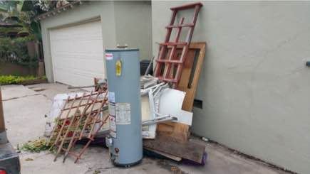 Hot water heater and mixed junk staged beside a garage for pickup