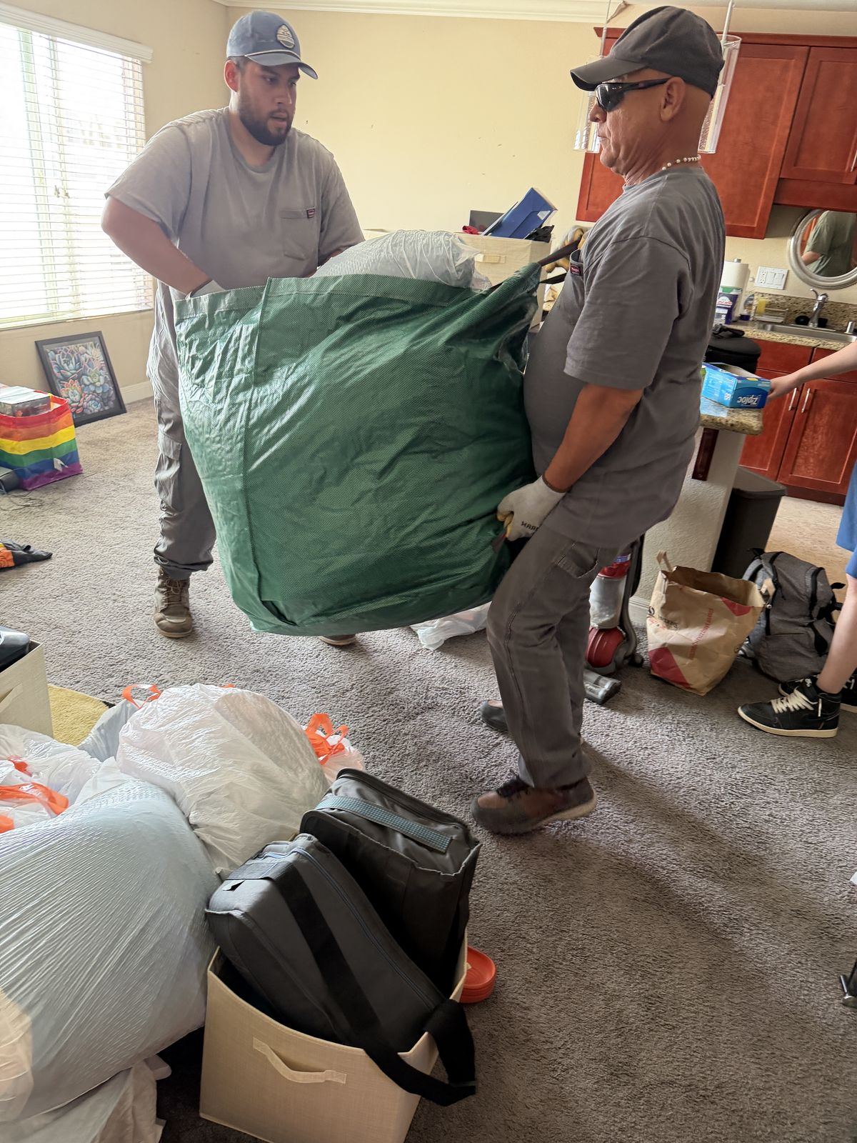 Two-person crew carrying a full bag of household junk through a San Diego living room