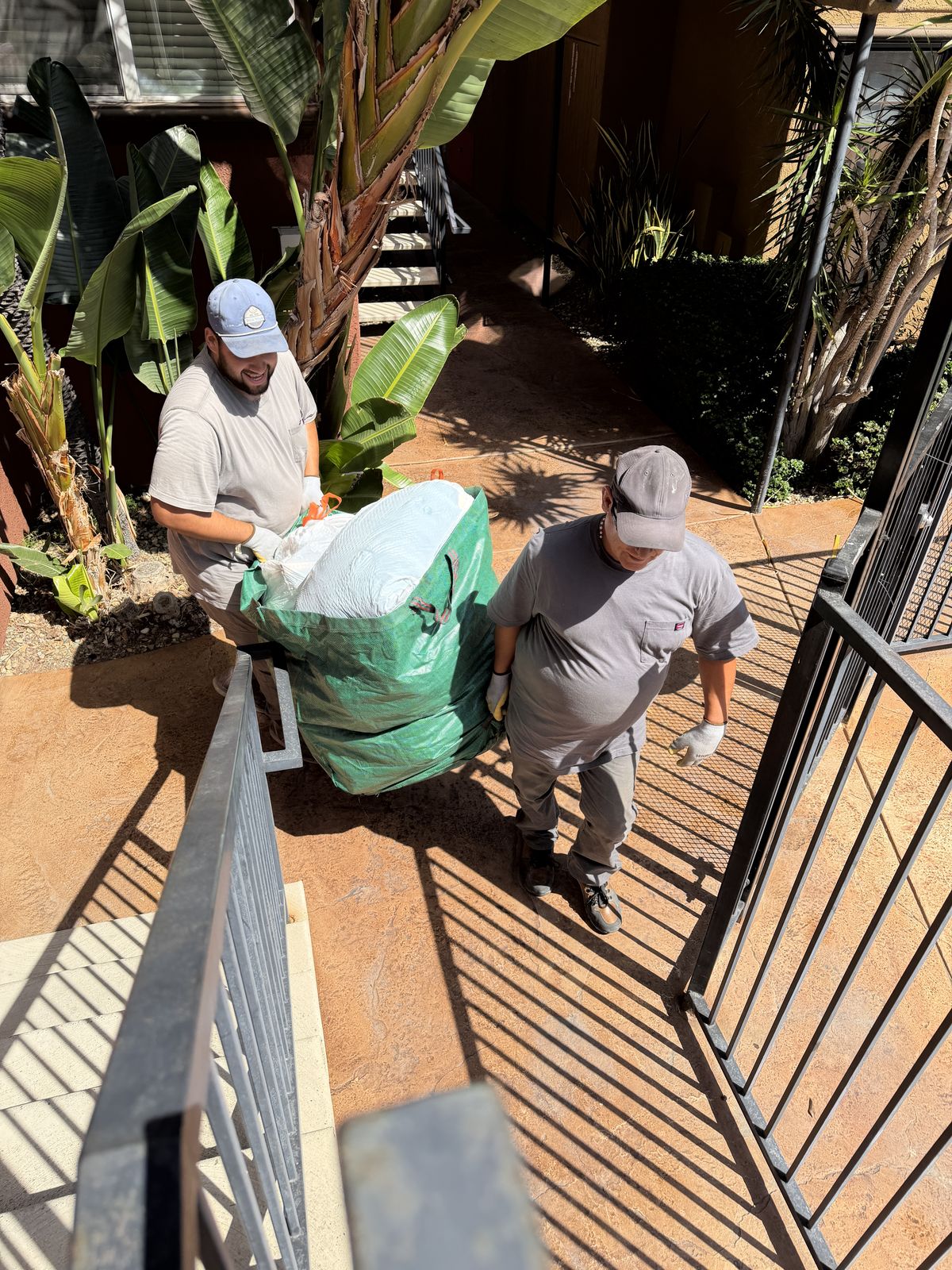 Crew walking a loaded junk bag out of a San Diego apartment walkway on a full-service haul