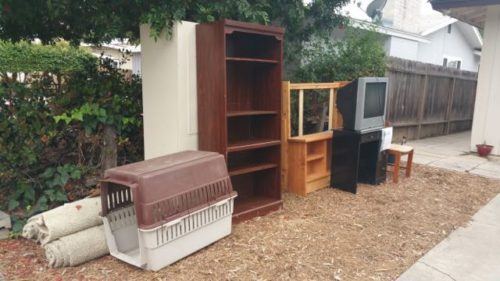 Bookshelf, TV stand, and mixed furniture in a side yard for haul away
