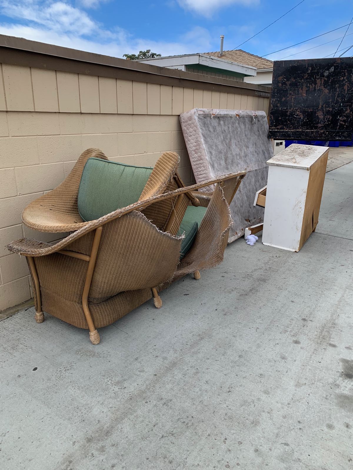 Worn wicker sofa, mattress, and dresser at the curb for hauling