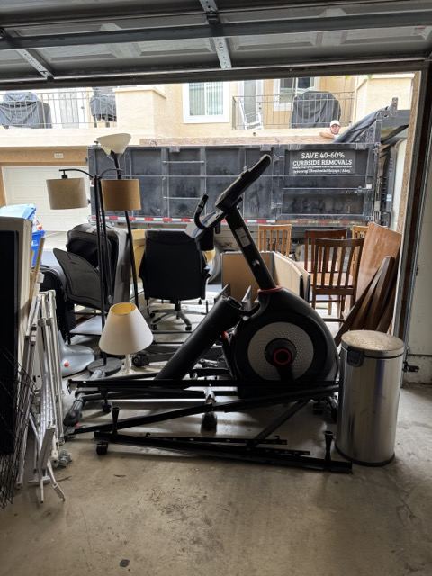 Garage loaded with an elliptical, chairs, and lamps for junk hauling