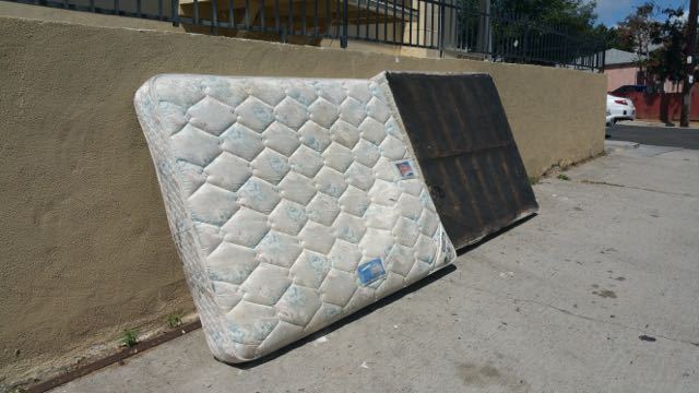 Quilted queen mattress and box spring leaning on a wall for curbside removal