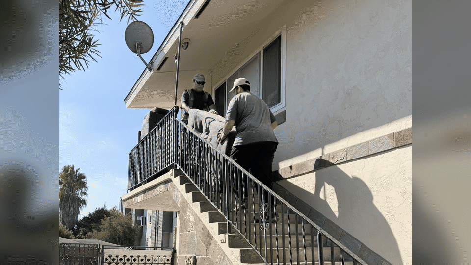 Full-service sectional sofa removal in University Heights, San Diego. Two men carry a two-piece gray sofa down outdoor apartment stairs.